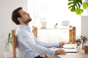 A man taking a deep breath as he sits in a home office.